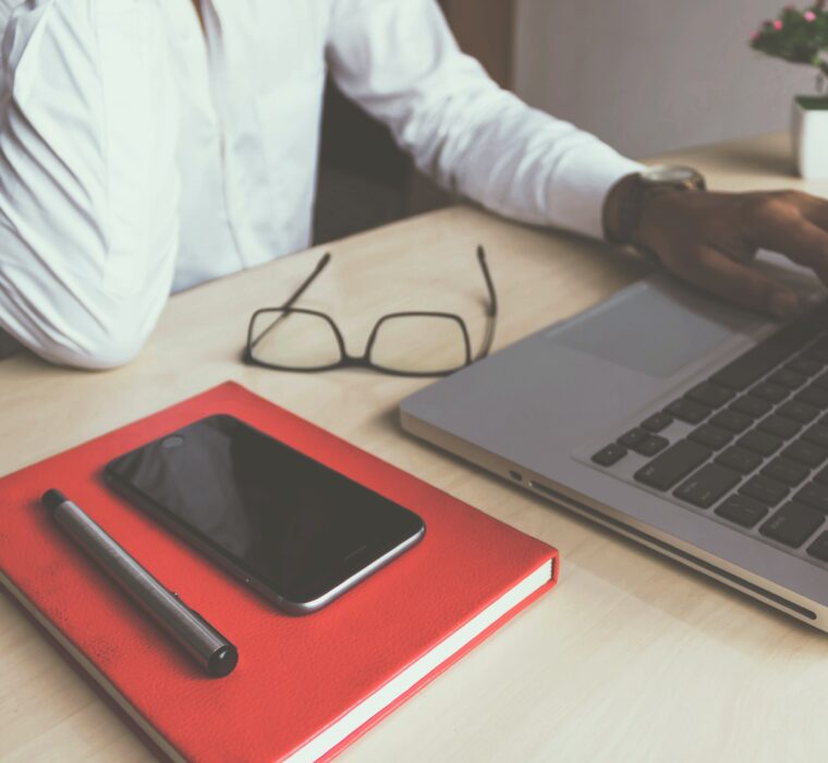 man at laptop with glasses on desk and notebook