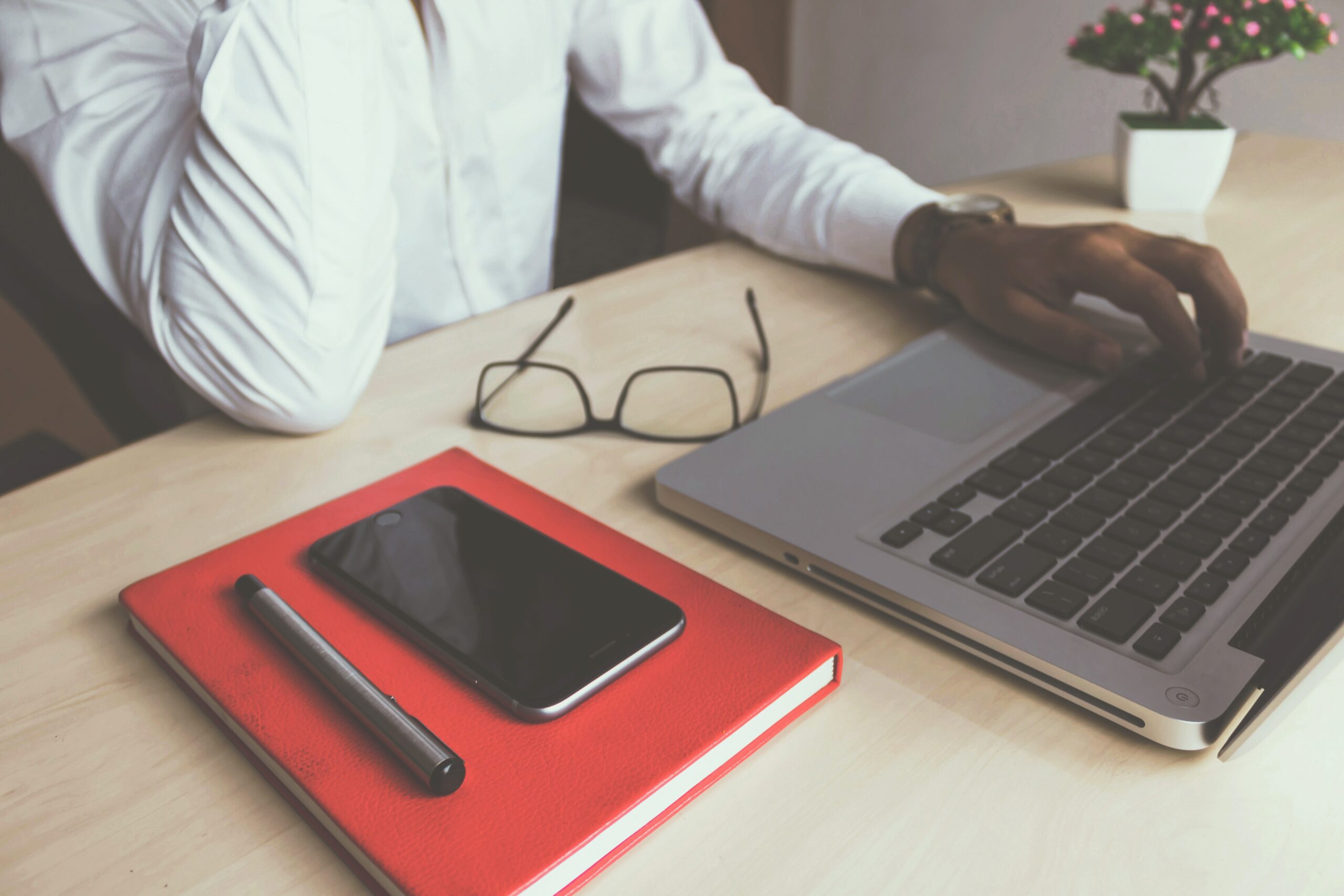 man at laptop with glasses on desk and notebook