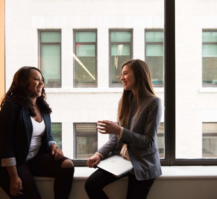 two women with notebooks talking in an office by a window