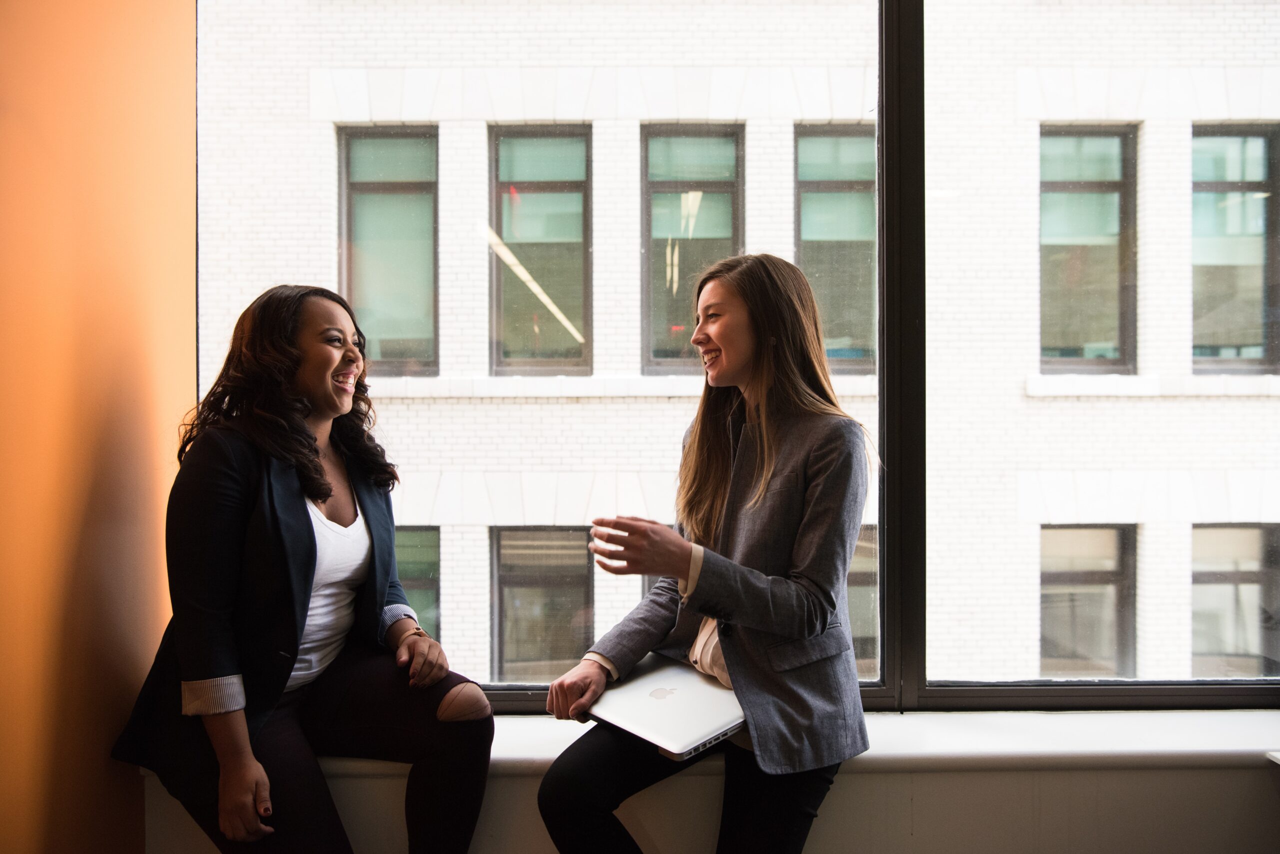 two women with notebooks talking in an office by a window