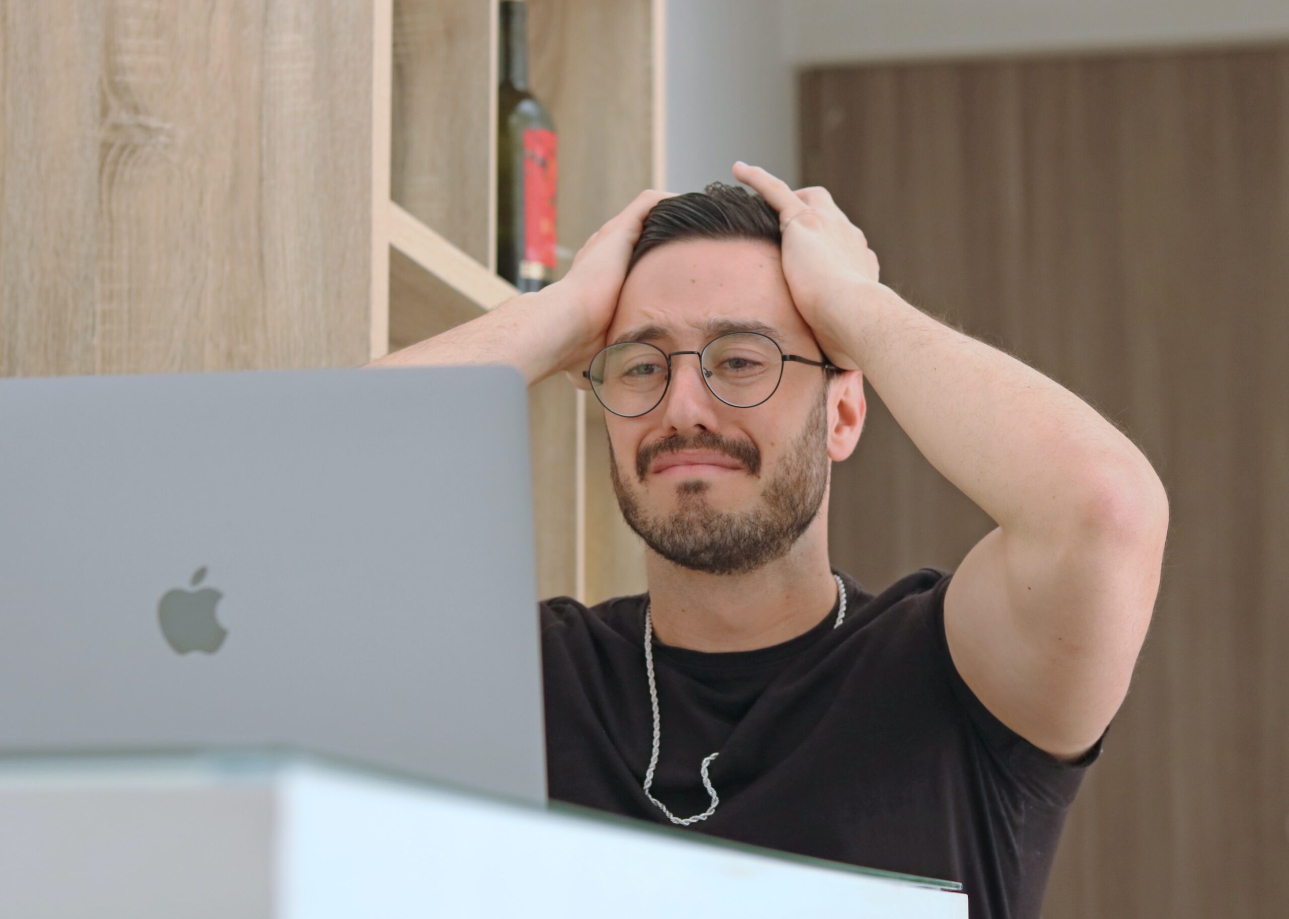 man holding his head in his hands and looking frustrated at computer