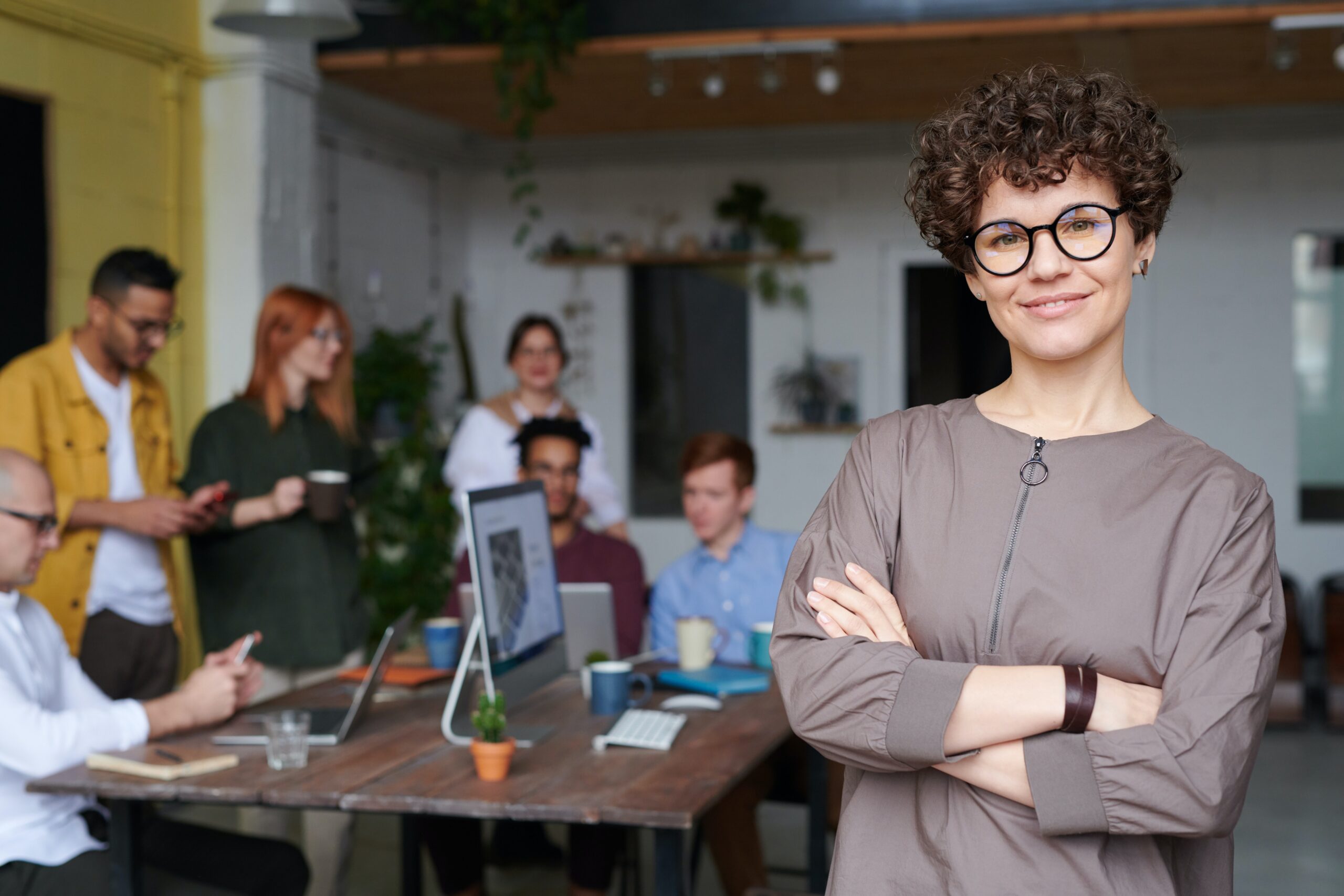group of people gathered around a desk and laptop with one woman smiling at camera wearing glasses