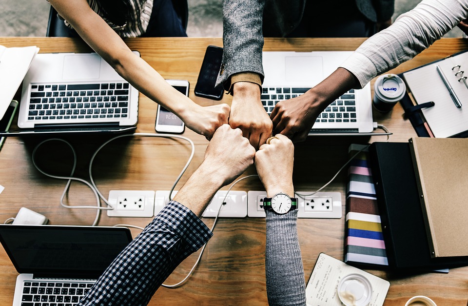 Fist bump with 5 people over a table with laptops